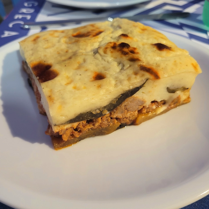 Porzione di moussaka calda con strati di melanzane, carne macinata e una spessa copertura di besciamella dorata