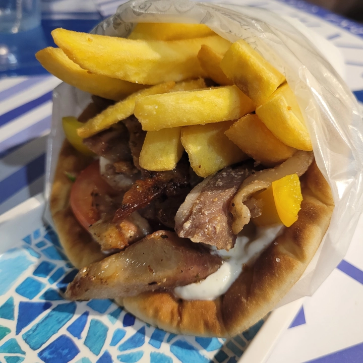 Pita greca ripiena di carne gyros, patatine fritte, pomodoro, cipolla e salsa tzatziki.